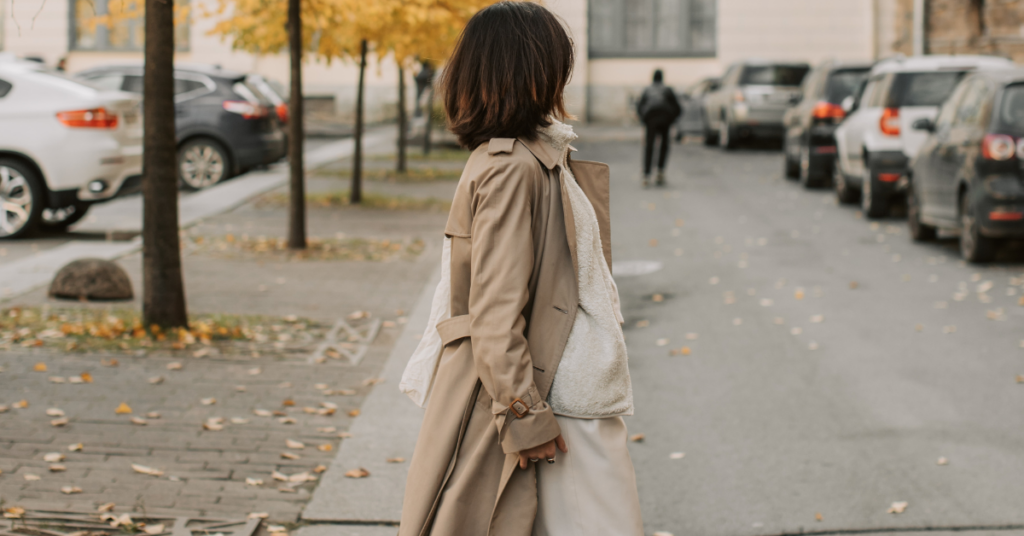 A woman in a chic trench coat stands on a quiet autumn street while looking away from the camera
